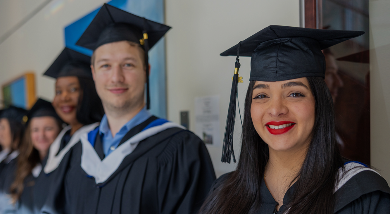 Two graduates wearing cap and gown, smiling at the camera