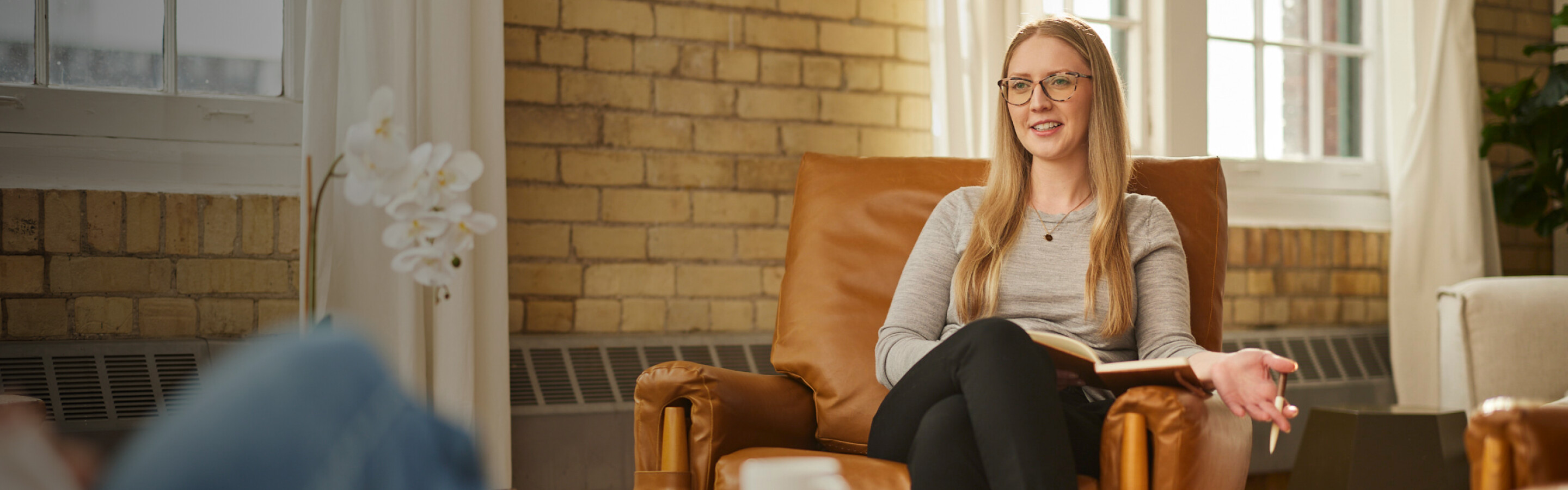 Woman sitting in a leather chair talking to a woman out of frame with a coffee table in between them